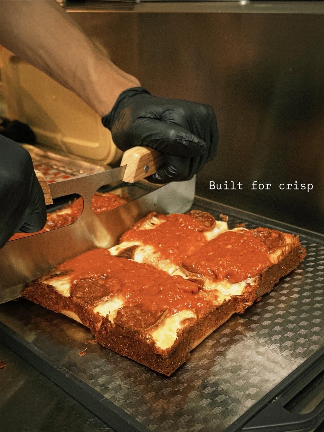 Pizza maker slicing a Detroit-style square pizza in Chiang Mai